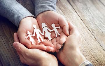 Two pairs of hands cupping a paper cut out of a family